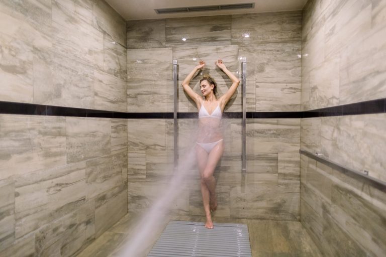 Young woman having high pressure shower after the treatment wrapping procedure at the modern spa salon